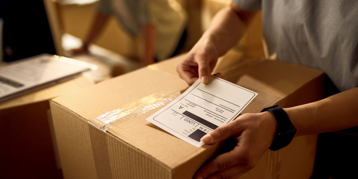 wp-5514e42d8143ff1c-closeup-courier-attaching-address-label-package-while-working-office