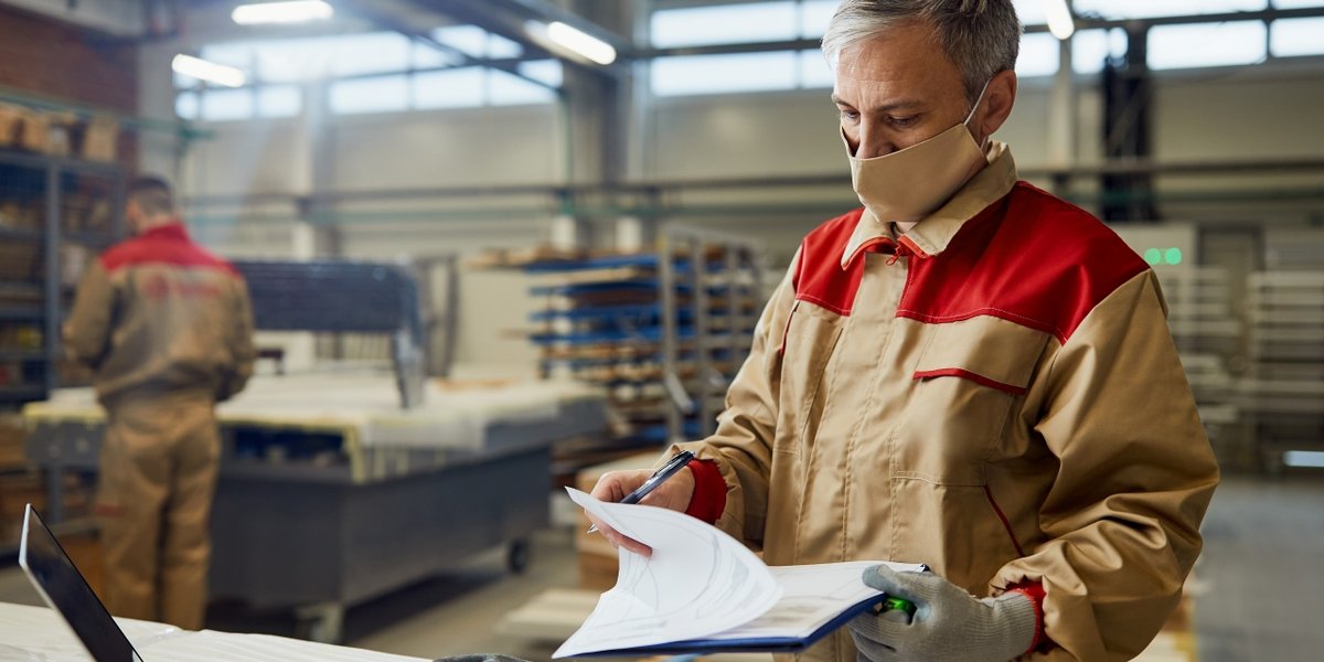 wp-680e583bc9e55c90-male-carpenter-wearing-face-mask-while-going-through-paperwork-workshop