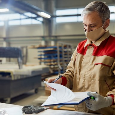 wp-680e583bc9e55c90-male-carpenter-wearing-face-mask-while-going-through-paperwork-workshop