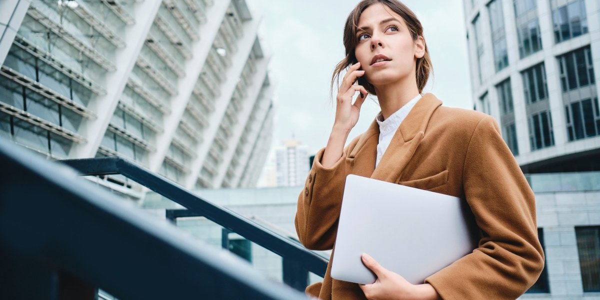 wp-774ed32380b5e435-young-pensive-casual-businesswoman-coat-with-laptop-talking-cellphone-thoughtful